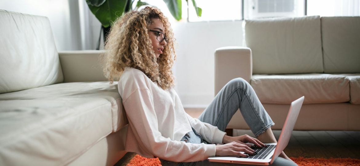 woman sitting on floor and leaning on couch using laptop